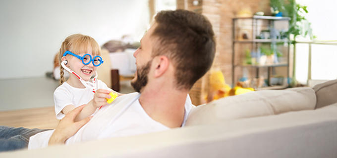 Man sitting on sofa with child using a toy stethoscope listening to the heart