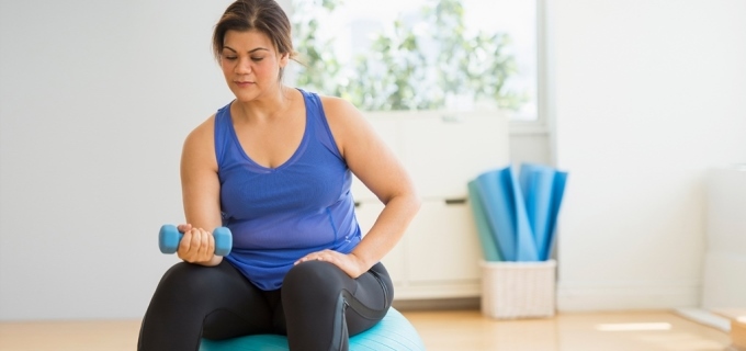 Woman sitting on a yoga ball lifting a weight